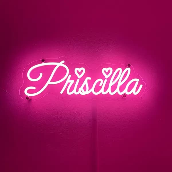 Hot pink 'Priscilla' script neon name sign with two small hearts on a pink-lit bedroom wall