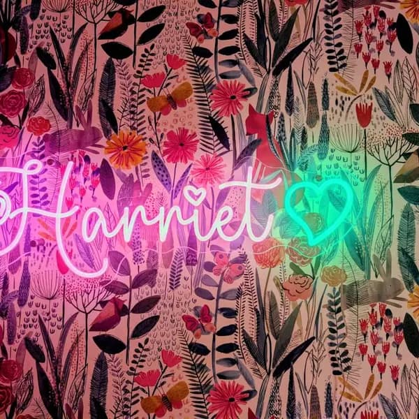 Pink 'Harriet' neon name sign with a teal heart on floral nursery wallpaper