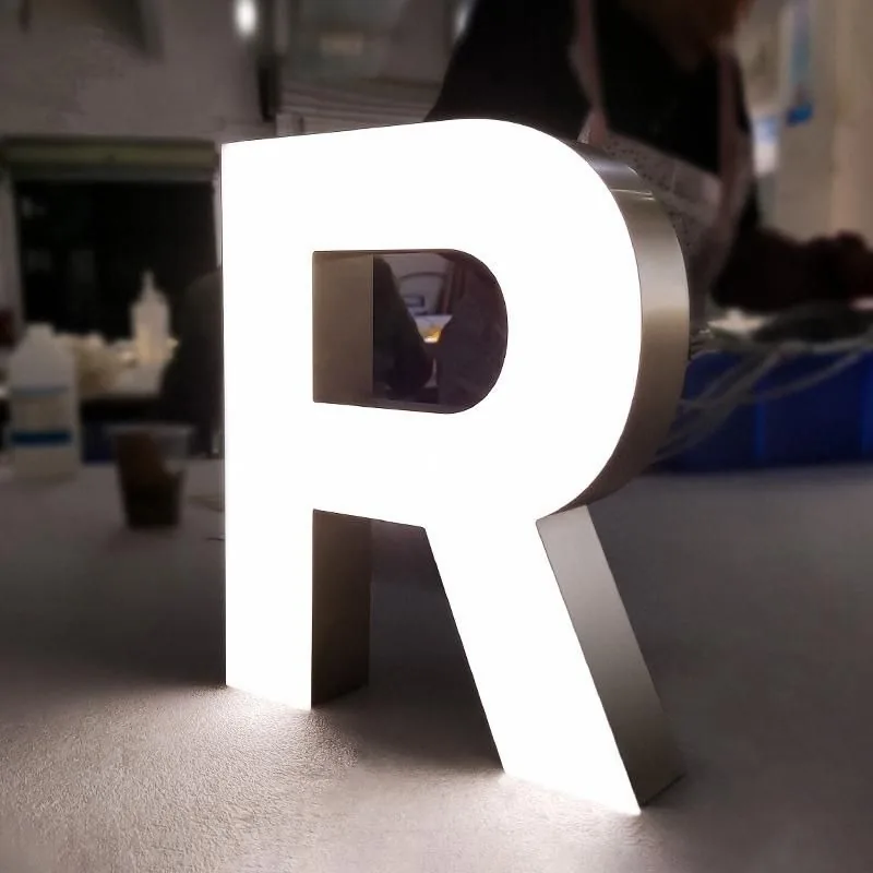 Fabricated stainless-steel channel letter R with a glowing white face and brushed metal returns
