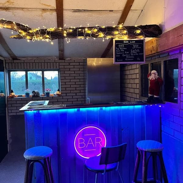 A warm amber-gold custom LED neon bar sign glowing above a bottle shelf in a cocktail lounge